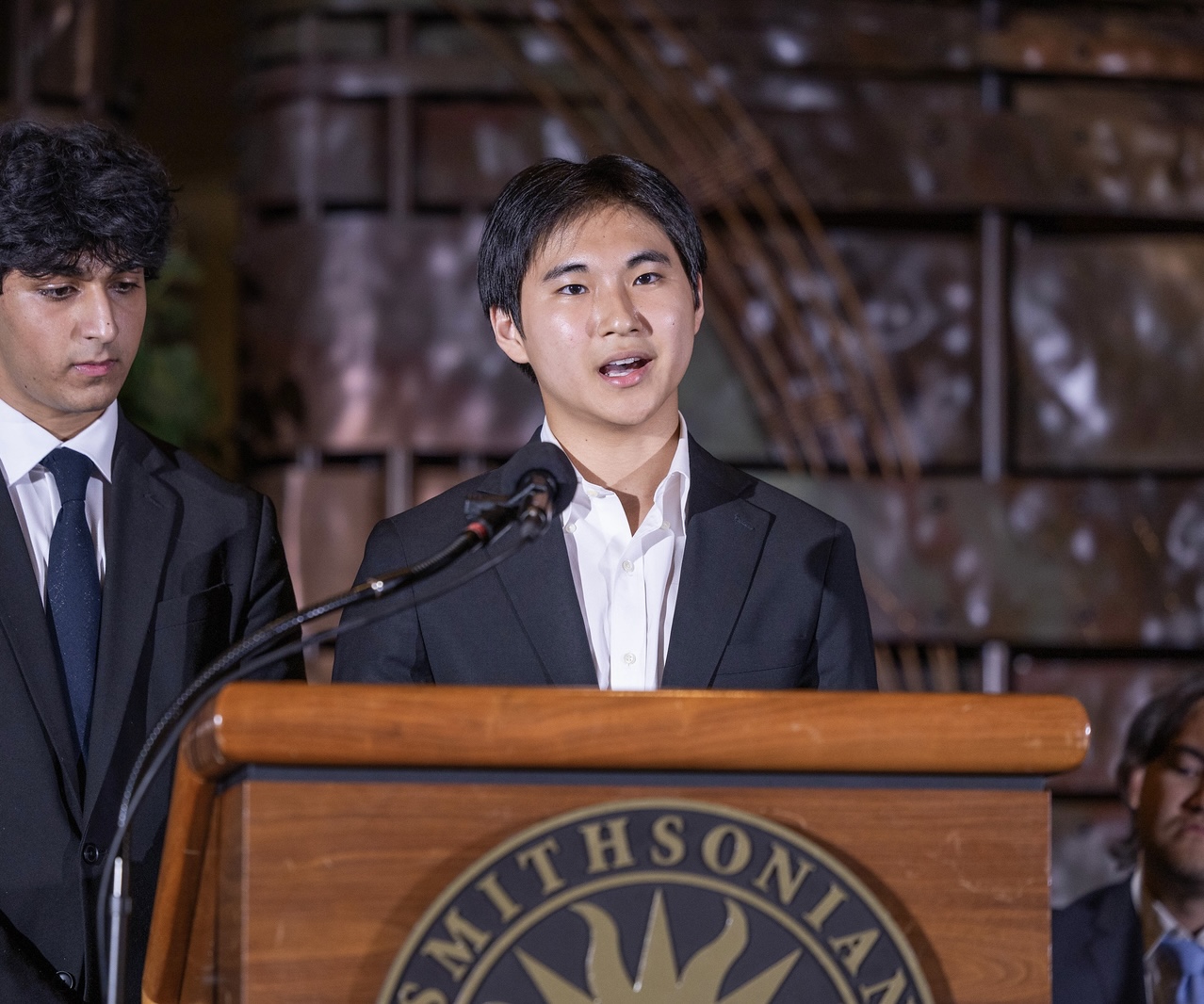 A photo of Philip speaking at a podium in the Smithsonian Museum of the American Indian for the Davidson Fellows Scholarship ceremony.